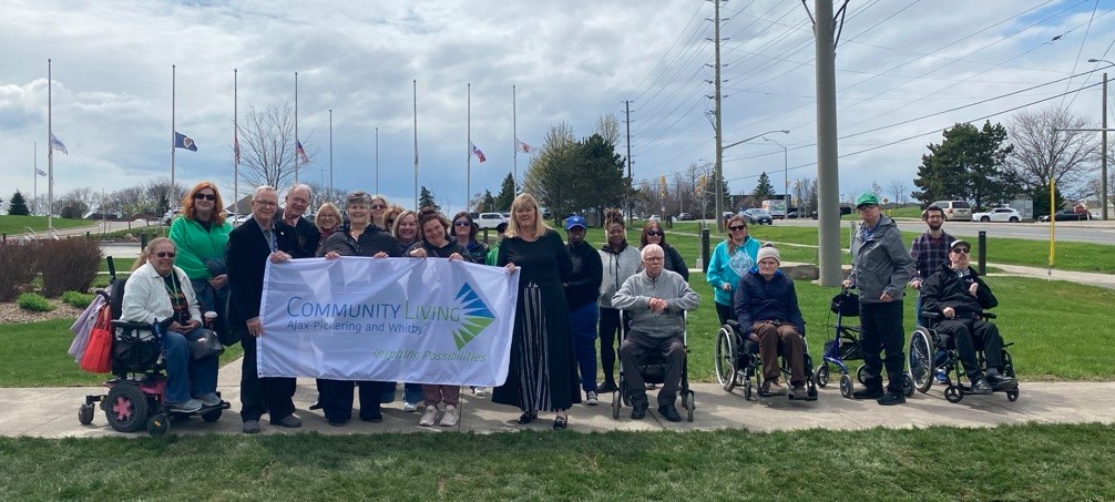 Durham elected officials, community partners from Community Living chapters, and community members holding the Community Living Month flag at Regional Headquarters. 