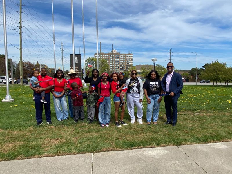 A group shot in front of the flagpoles with attendees at the Haitian Flag Day proclamation ceremony